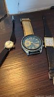 Three watches laid side by side on a wooden surface showing different styles and strap types