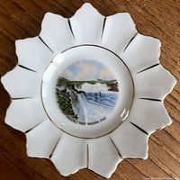 Top view of white porcelain dish with 13 scalloped points and central image of Niagara Falls labeled 'Prospect Point Niagara Falls'. Edges trimmed in gold.