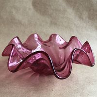 Side view showing the ruffled edges and translucent cranberry pink glass with swirl design.