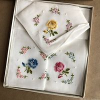 Set of three vintage cotton handkerchiefs displaying detailed hand embroidery of roses in yellow, blue, and red, along with surrounding small flowers and white embroidered dots, neatly folded in original gift box.