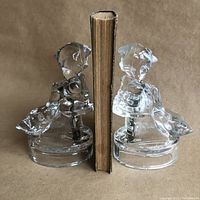 Front view showing two clear glass figurines acting as bookends holding an old book.