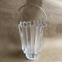 Side view of clear heavy textured glass ice bucket with vertical bubble-like ridges and semi-circular chrome handle, placed on brown paper background.