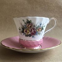 Side view of teacup and saucer showing floral pattern, pink base, and gold trim on teacup with ruffled pink saucer