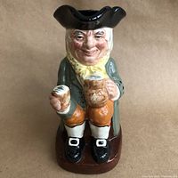 Front view of the ceramic toby mug figurine showing a seated character with a tricorn hat, holding a beer mug and pipe, colorful detailed painting.