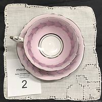 Top-down photo showing the interior pale pink wash and floral band of the tea cup set against a white embroidered cloth.