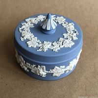 Angled top view of the vintage Wedgwood jasperware covered trinket box showing blue base and creamy white grapevine decorative reliefs around lid and knob handle.