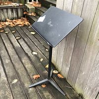Photo of the full black Wenger music stand outdoors showing the three-legged base on a wooden deck with fallen leaves around.