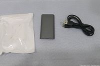 Photo showing 2TB external hard drive, USB cable, and packaging pouch on a gray cloth.