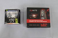 Photo showing two automotive headlight bulb packages side by side. Left is a Sylvania SilverStar zXe H13 halogen bulb package containing two bulbs. Right is an Ignite LED H11 performance bulb box.
