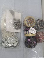 Photo of candle making accessories including bundles of candle wicks with metal tabs and decorative tealight candle holders with colorful designs.