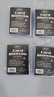 Four packs of BCW card sleeves arranged on a surface, showing front of packaging with branding and text.