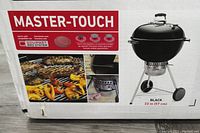 Box front showing Master-Touch branding, Gourmet BBQ System logo, grilled food imagery and 'Black 22 in (57 cm)' label