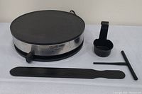 Photo of Presto electric crepe maker with spreader, batter ladle, and batter spreader tool set on white cloth