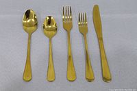 Flatware pieces arranged to show each type: tablespoon, teaspoon, dinner fork, salad fork, and dinner knife, all gold-colored and unused.