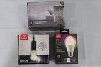 Photo of three boxed lighting items: a box of LED colour changing string lights, a globe Edison-style bulb box, and a globe smart LED bulb box.