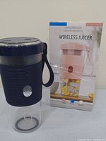 Photo of a blue portable wireless juicer blender next to its retail box showing a pink model.