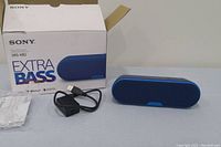 Sony SRS-XB2 Bluetooth speaker in blue with original box, charger, and user manual on display against a gray background.
