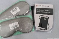 Photo of two grey padded eye masks with mint green edges along with an Air Canada branded black neck money holder in packaging.