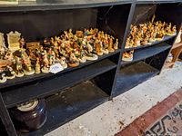 Two black shelves densely packed with painted porcelain Sebastian Studio figurines, assorted characters and small scenes visible