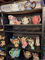 Four shelves of mostly ceramic teapots, pitchers, and planters in various shapes and colors, including animal forms.