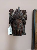 Frontal view of the dark wooden carved Asian wall mask showing facial details and headdress