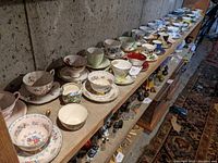 Full-length view of two shelves displaying over 30 teacup and saucer sets in assorted patterns
