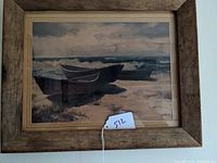 Framed print showing three boats on the sand by the ocean and cloudy sky. Rustic wooden frame visible.