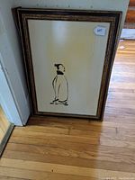 Full view of framed print leaning against wall on hardwood floor