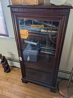 Full view of the dark wood display cabinet showing glass front door, decorative wood trim, and bracket feet.