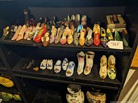 Shelf display showing dozens of miniature shoes of varied styles, some with floral patterns and painted designs, a small boxed shoe visible.