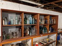 Overall view of wooden shelving unit with six compartments containing assorted glass bottles and insulators