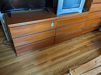 Full view of long, low mid-century teak dresser with six horizontal drawers, showing the wood grain and design style.