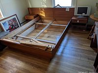 Overall view of the partially disassembled teak platform bed frame with headboard, side rails and two floating nightstands attached.