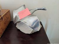 Top angle showing metal loon sculpture from above, highlighting wing curvature and stone base surface.