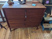 Front view of a four drawer teak dresser showing reddish-brown wood grain finish with keyholes and round wooden knobs.