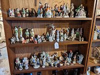 Three wooden shelves filled with approximately 60 small to medium porcelain figurines in colorful historic and ethnic dress, displayed close together.