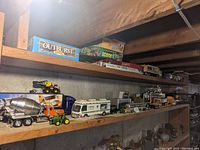 Two wood shelves holding boxed board games on top and assorted die-cast vehicles below