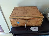 Front view of the jewelry box showing the bird's-eye maple surface, decorative banded inlay, and lock with key in place.