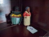 Photo showing two cast iron figurines, the door stop with yellow and green clothing and the still bank as a woman with a blue headscarf and red dress.