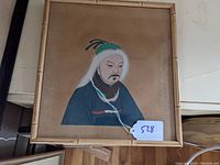 Frontal view of the framed portrait showing the subject in traditional attire and green hat on a beige background.