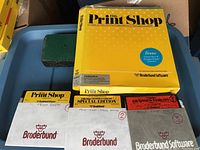 Yellow boxed Print Shop software with accompanying floppy disks including The Print Shop, Special Edition Graphics Library and Graphics Library disks with labeled sleeves.