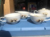 Three tea cups with pine cone design and gold rim placed side by side
