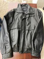 Black Pelle Cuir leather jacket in good condition lying flat, showing front details with snap buttons and pockets.
