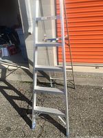 Front view of the Reynolds aluminum ladder showing steps and structure, placed outdoors near orange storage doors.