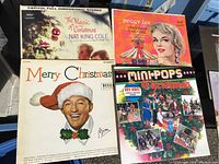 Photo of four Christmas-themed vinyl records with covers showing Nat King Cole, Peggy Lee, and another Merry Christmas cover.