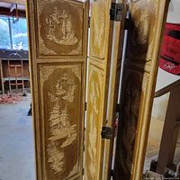 Side angle of four-panel wooden screen showing carved Asian scenes of boats and nature with visible wear and fading.