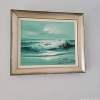 Framed acrylic painting of waves breaking on shore hanging on wall, showing full artwork and frame.