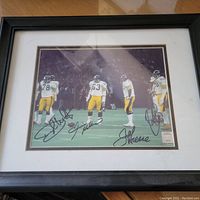 Framed autographed photo of four Pittsburgh Steelers players on the field with visible autographs