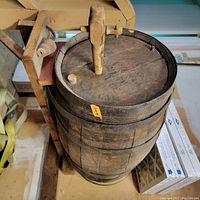 Top angle view of wooden barrel showing open top with wooden spout and stopper, detailing the loose metal ring around the top edge.