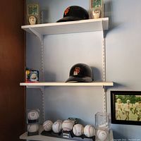 Shelves displaying 2 San Francisco Giants batting helmets, 7 baseballs with some in display cases, and baseball-themed memorabilia items.